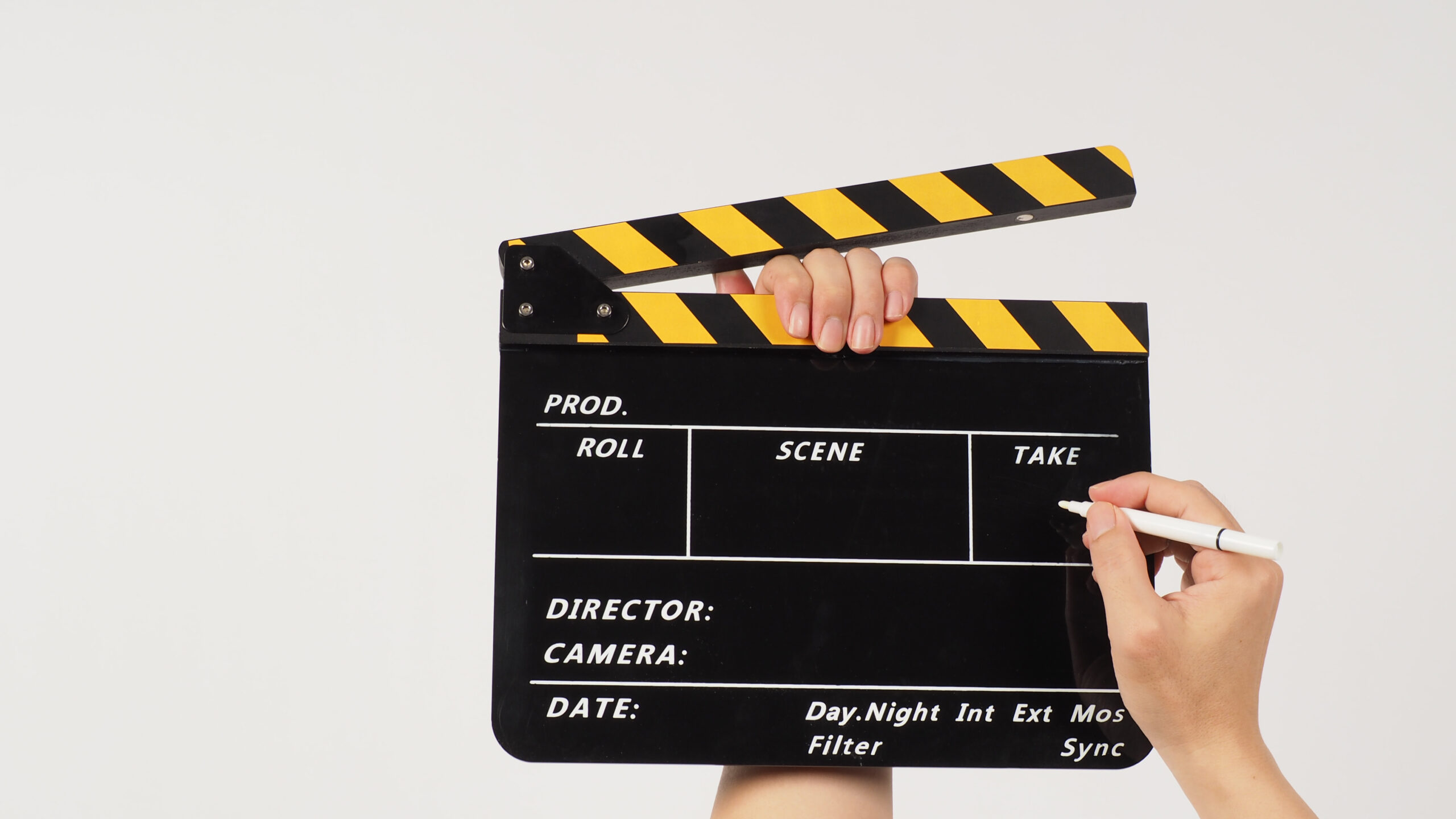 The hand is holding a yellow and black clapper board and marker